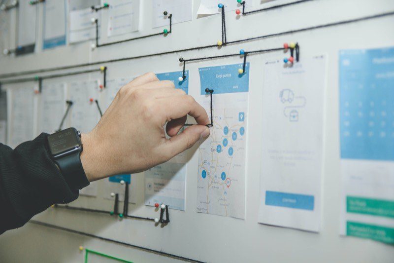 A hand pinning printed app screens to a board while planning a build