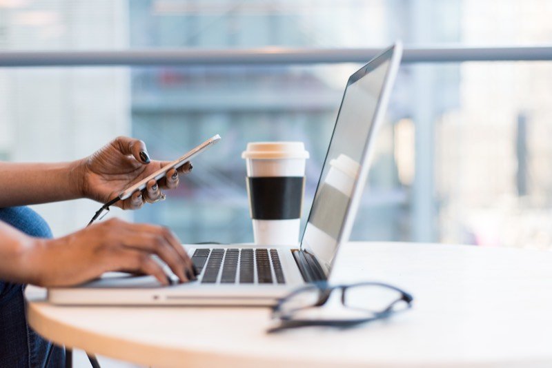 Someone working at a laptop with a phone in hand at a desk
